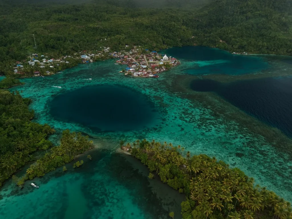 Pemandangan udara desa di Kepulauan Banggai dengan lubang biru di tengah terumbu karang, tujuan kapal dari Luwuk
