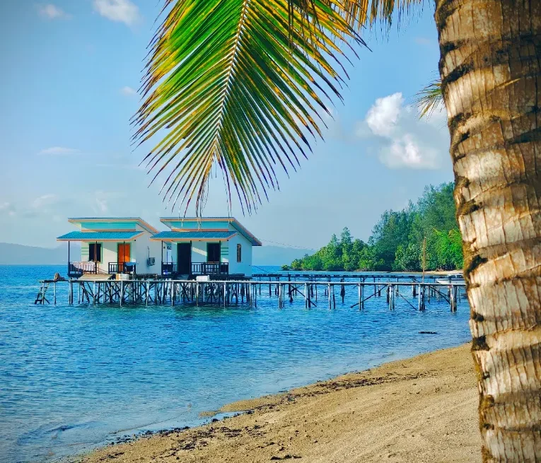 Overwater bungalows on stilts beside a white sand beach, accommodation in the Banggai Islands