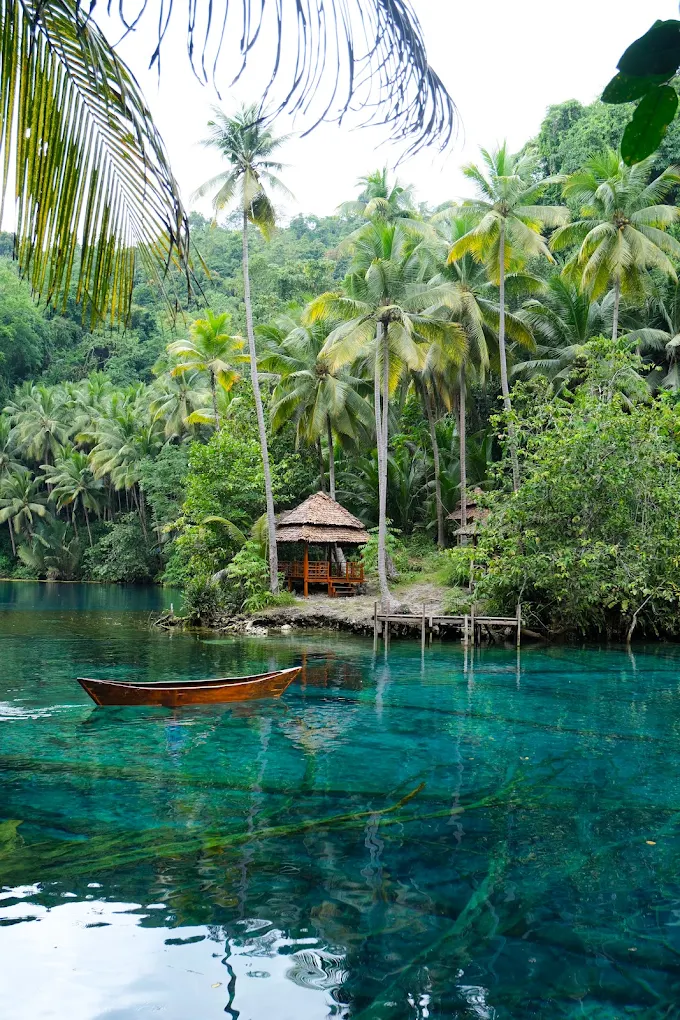Wooden canoe on the clear green water of Paisu Pok Lake beside a thatched hut, Banggai Islands