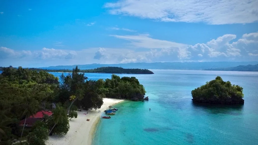 Aerial view of a small island with a white sand beach and red roofed guesthouse in the Banggai Islands