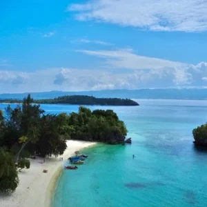 Aerial view of a small island with a white sand beach and a red roofed guesthouse in the Banggai Islands