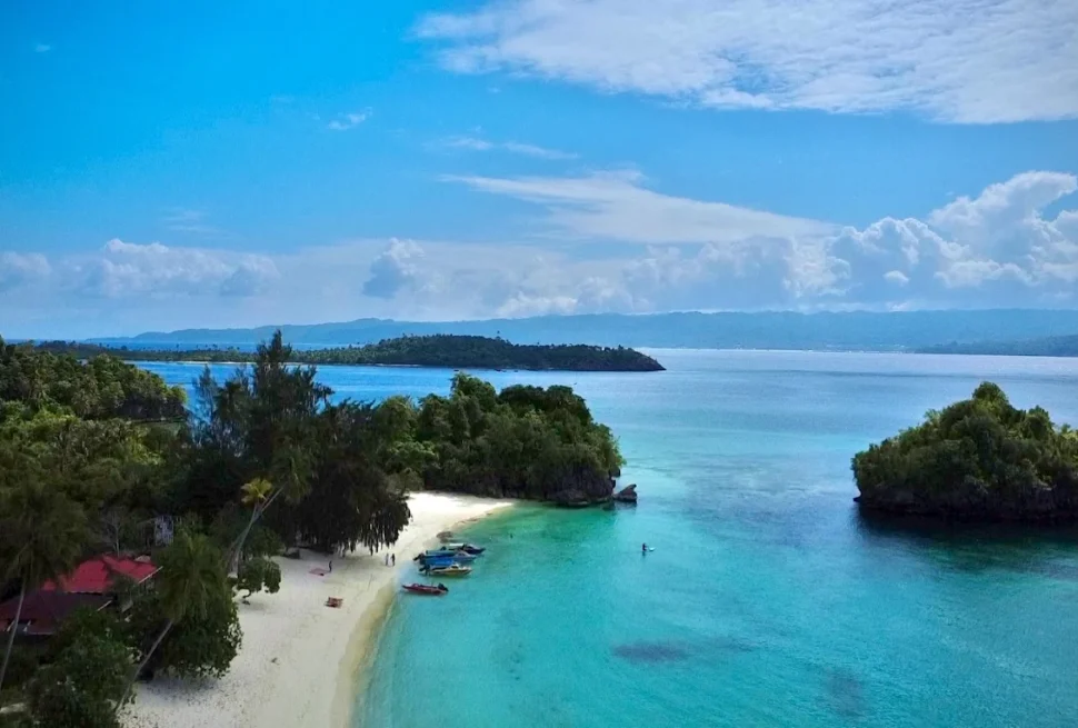 Aerial view of a small island with a white sand beach and a red roofed guesthouse in the Banggai Islands