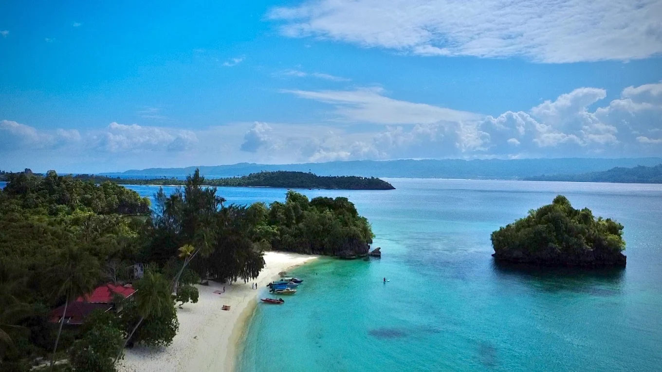 Aerial view of a small island with a white sand beach and a red roofed guesthouse in the Banggai Islands
