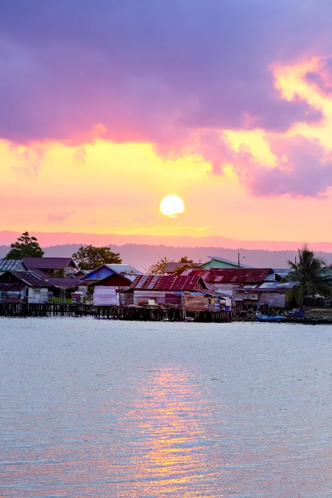 Matahari terbenam berwarna merah muda di atas kampung nelayan di atas air dekat Luwuk