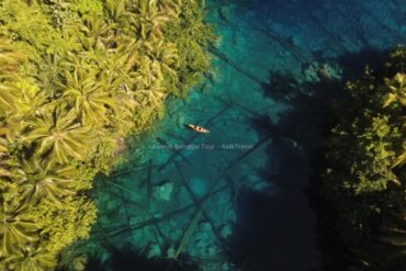 Perahu kayu kecil berisi dua orang di atas danau jernih penuh tanaman air