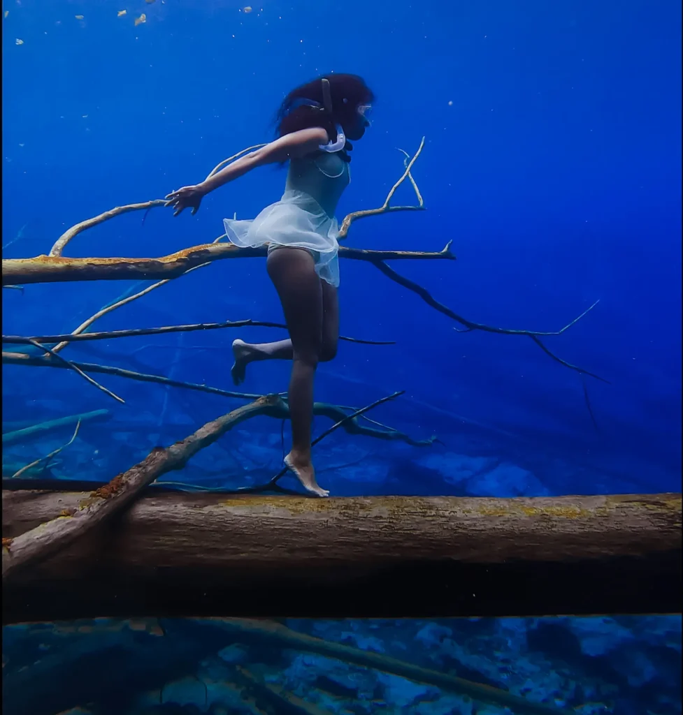 Free diver exploring Paisu Pok Lake underwater with fallen trees visible in crystal clear water of Banggai Islands Indonesia