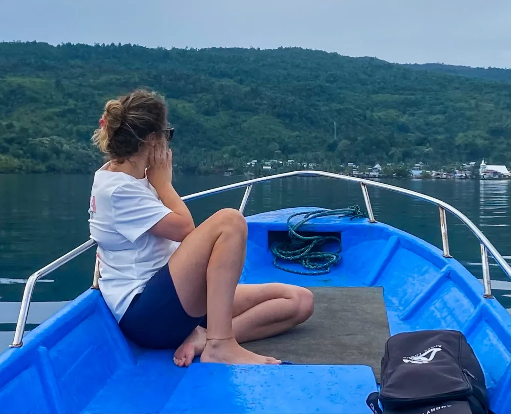 Traveler enjoying speedboat tour of Paisu Pok Lake with turquoise water, jungle-covered mountains, and traditional village in Banggai Islands Sulawesi