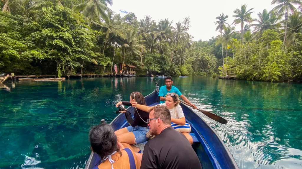 Group of tourists rowing wooden boat through Paisu Pok Lake with crystal clear turquoise water and tropical jungle canopy in Banggai Islands Sulawesi