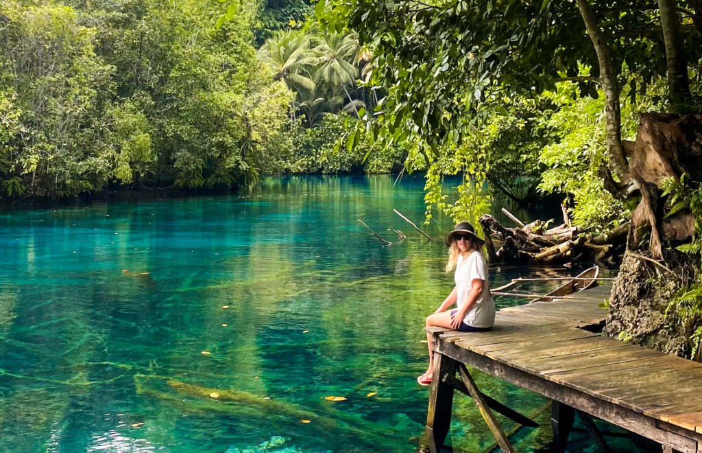 Visitor sitting on wooden boardwalk platform at Paisu Pok Lake overlooking pristine turquoise freshwater lake in Banggai Islands

