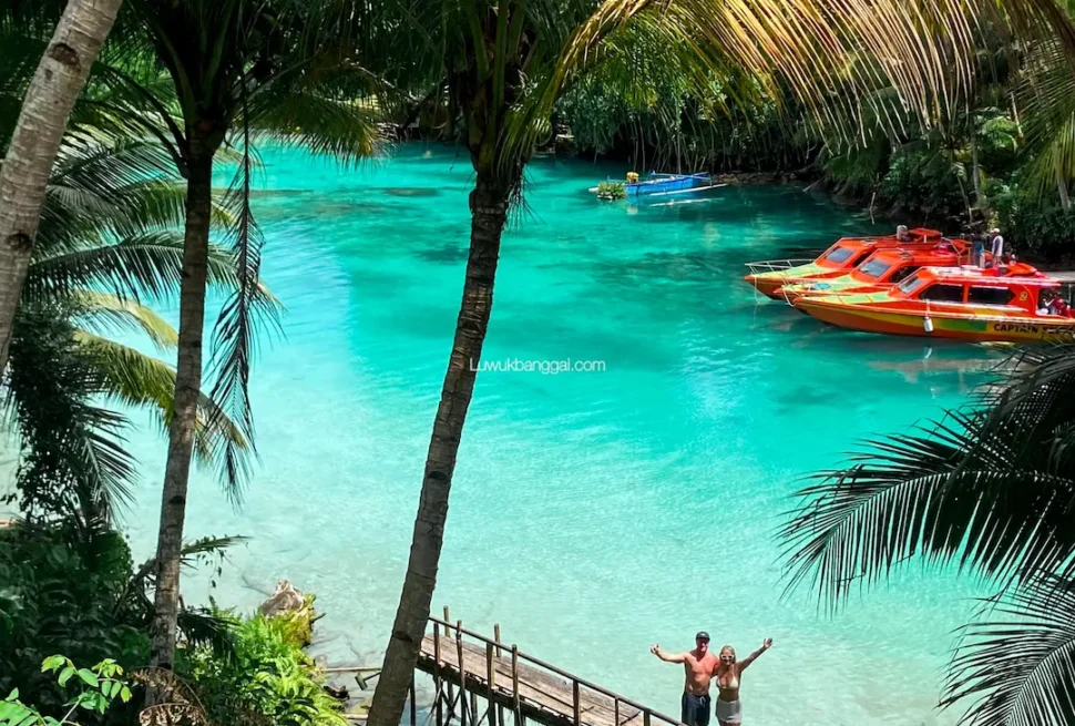Sepasang wisatawan berdiri di dermaga kayu menikmati pemandangan air jernih berwarna biru toska di Danau Paisupok Luwuk Banggai.