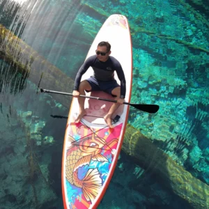 Paddleboarder floating over sunken trees in the clear water of Paisu Pok Lake on Peleng Island