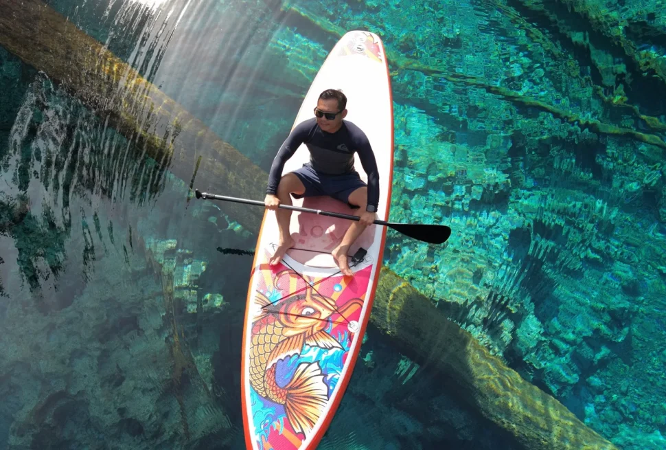 Paddleboarder floating over sunken trees in the clear water of Paisu Pok Lake on Peleng Island