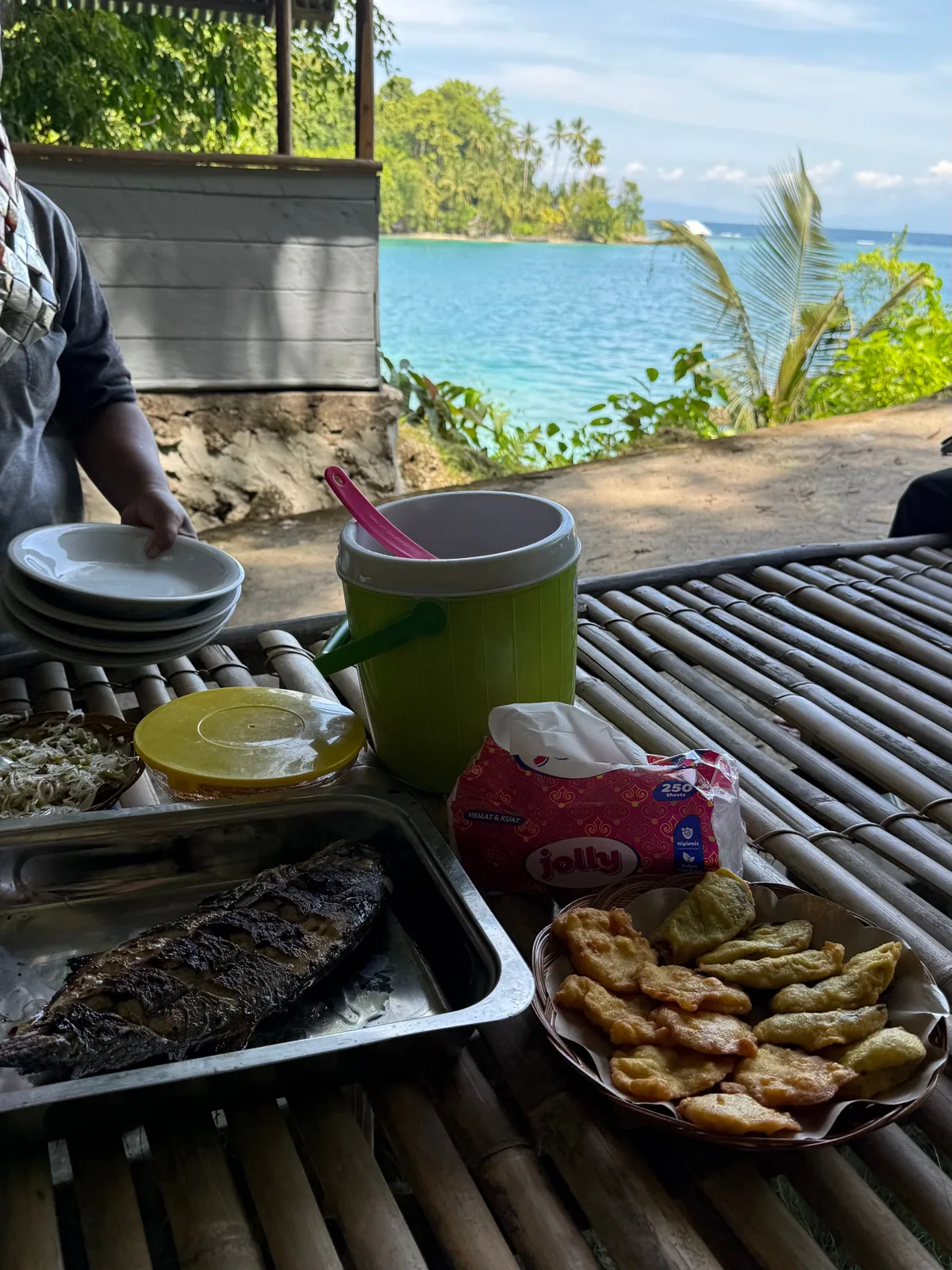 Ikan bakar, gorengan, dan minuman di meja bambu sebuah pondok tepi laut, Kepulauan Banggai