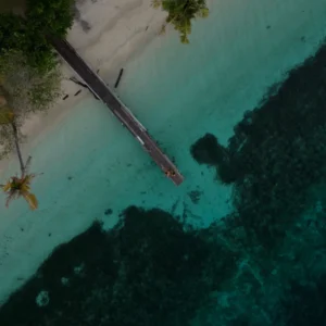 Foto udara pantai pasir putih dengan dermaga kayu dan terumbu karang di Kepulauan Banggai
