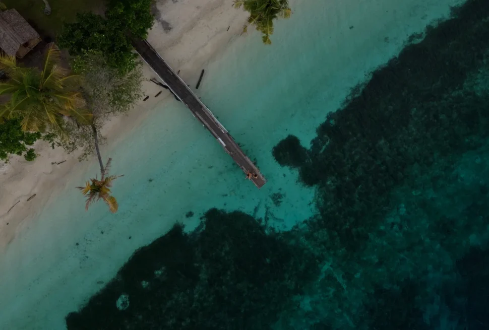 Foto udara pantai pasir putih dengan dermaga kayu dan terumbu karang di Kepulauan Banggai