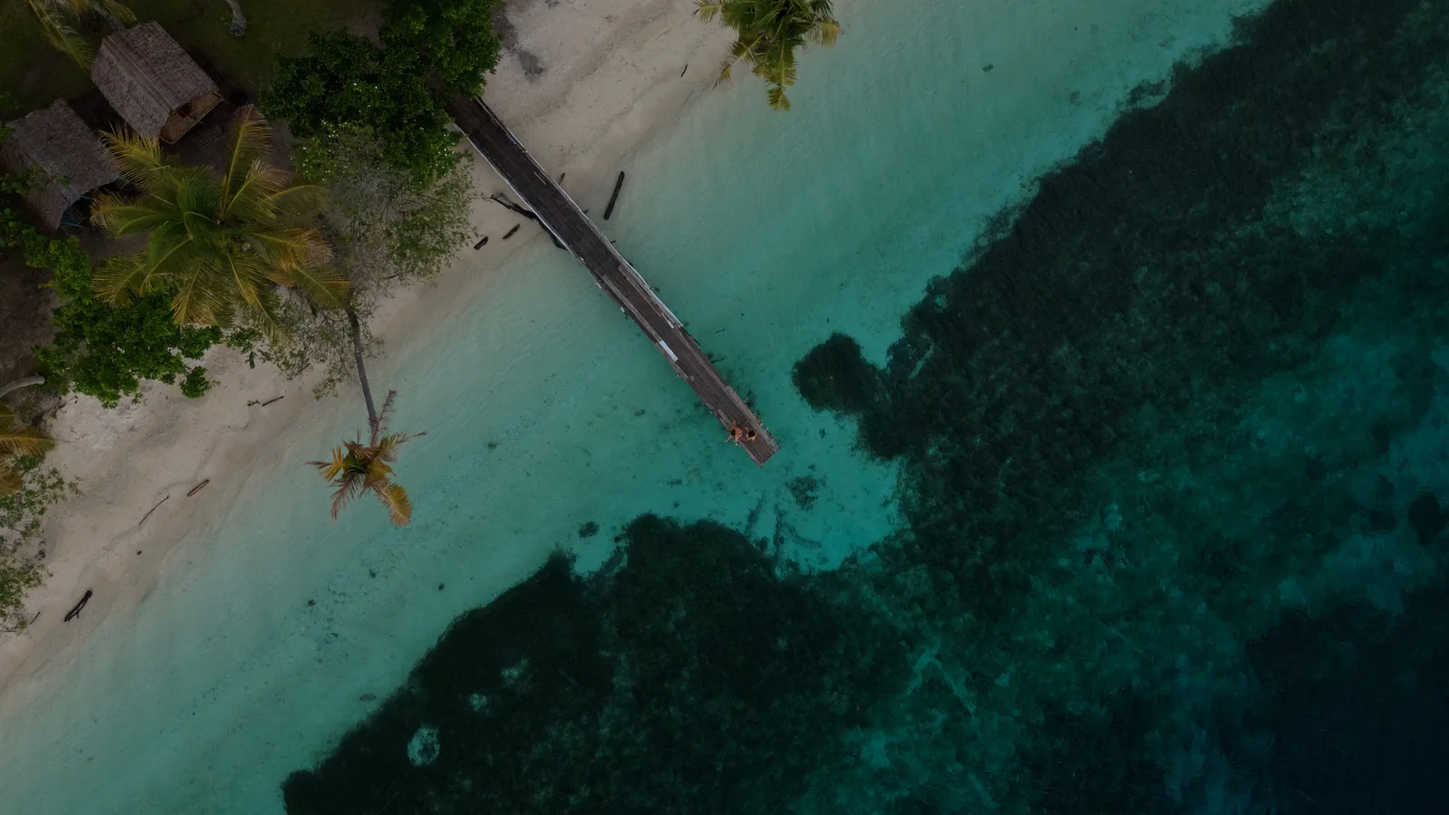 Foto udara pantai pasir putih dengan dermaga kayu dan terumbu karang di Kepulauan Banggai