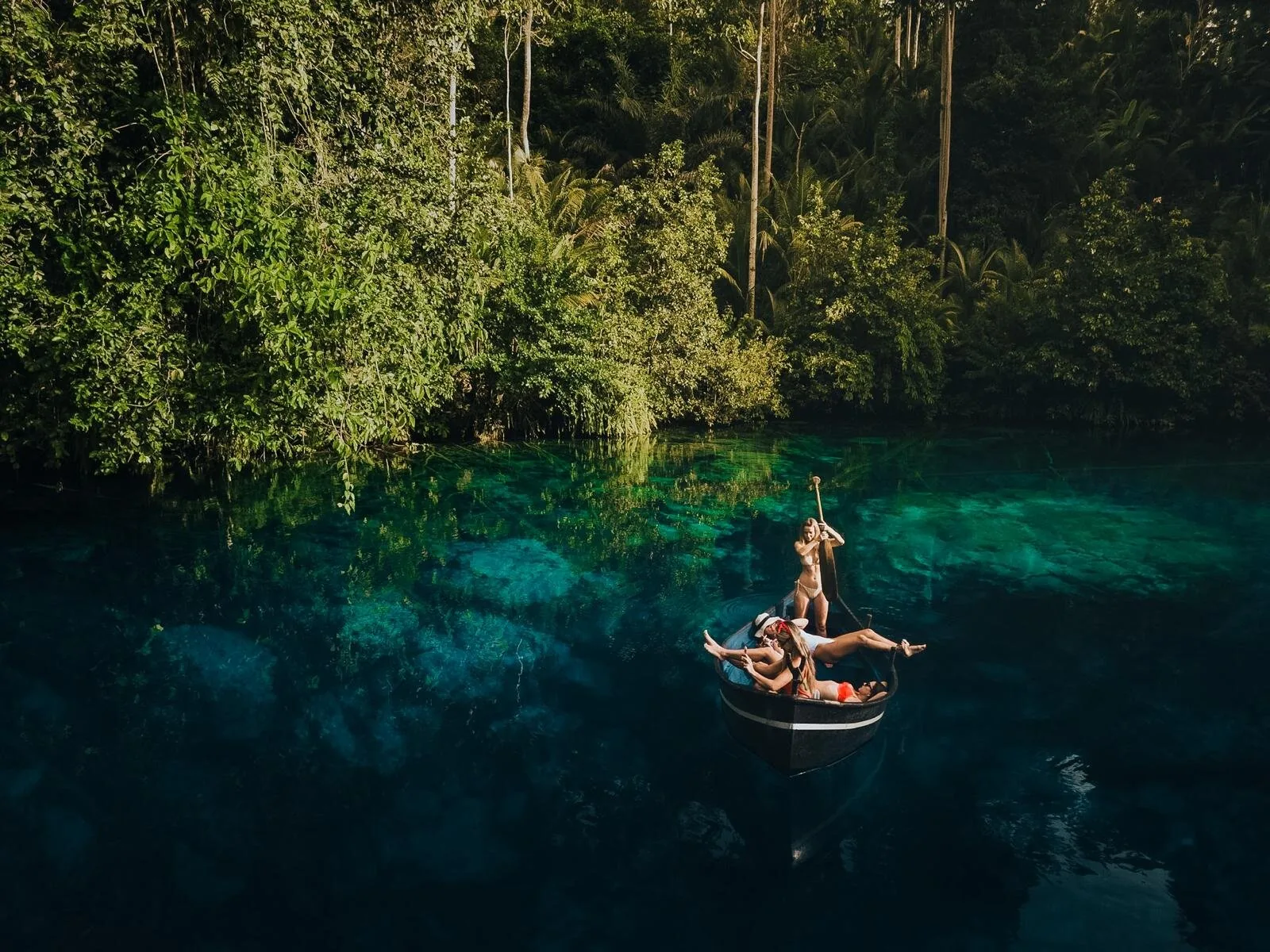 Wisatawan di atas perahu kecil di danau biru jernih yang dikelilingi hutan