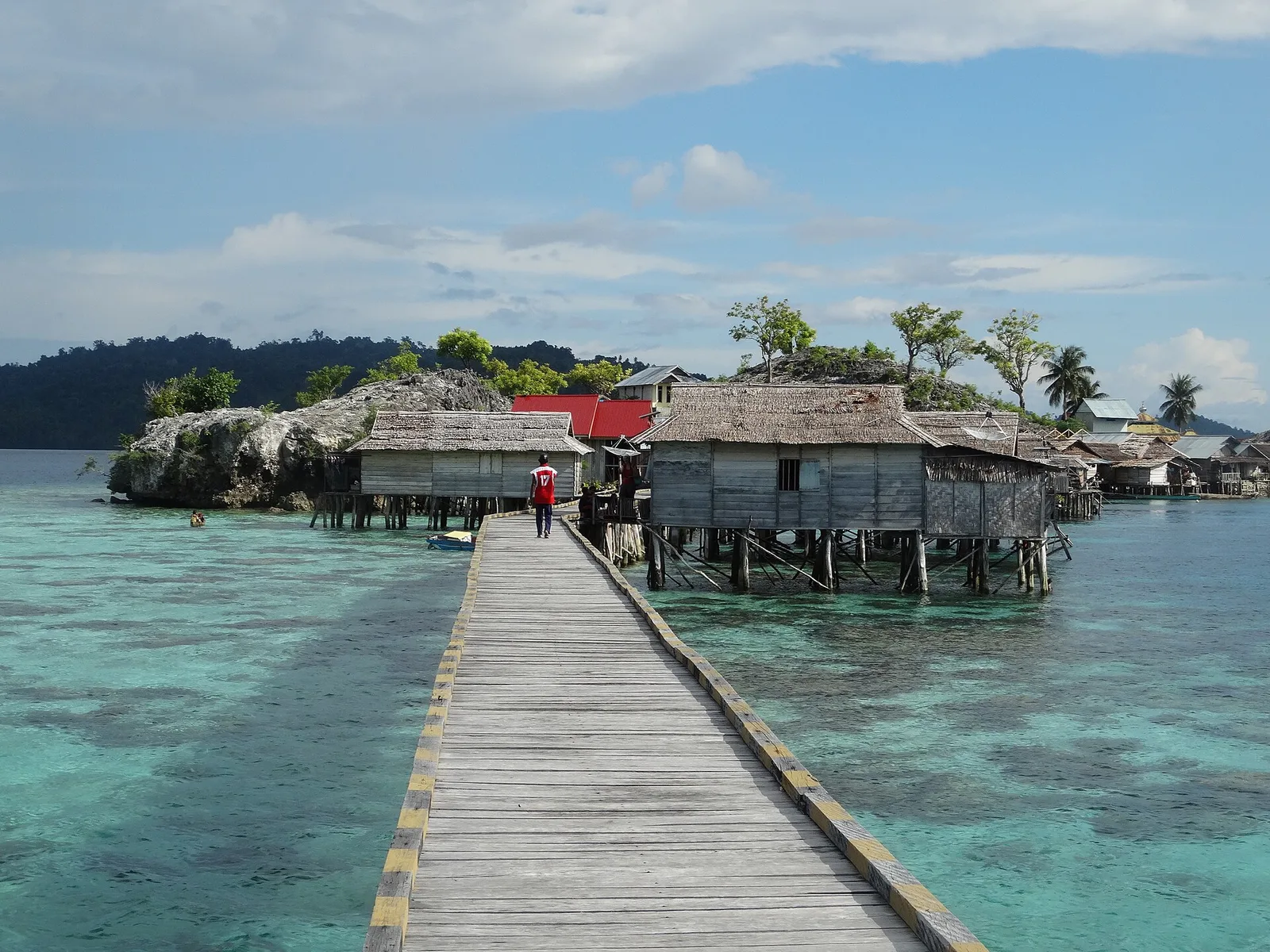Wooden walkway leading to Bajau stilt houses over clear water in Kabalutan, Togian Islands