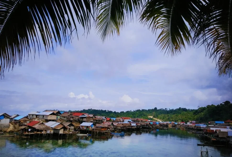 Paalwoningen van het dorp Kulingkinari tussen de palmbladeren door, Tojo Una-Una